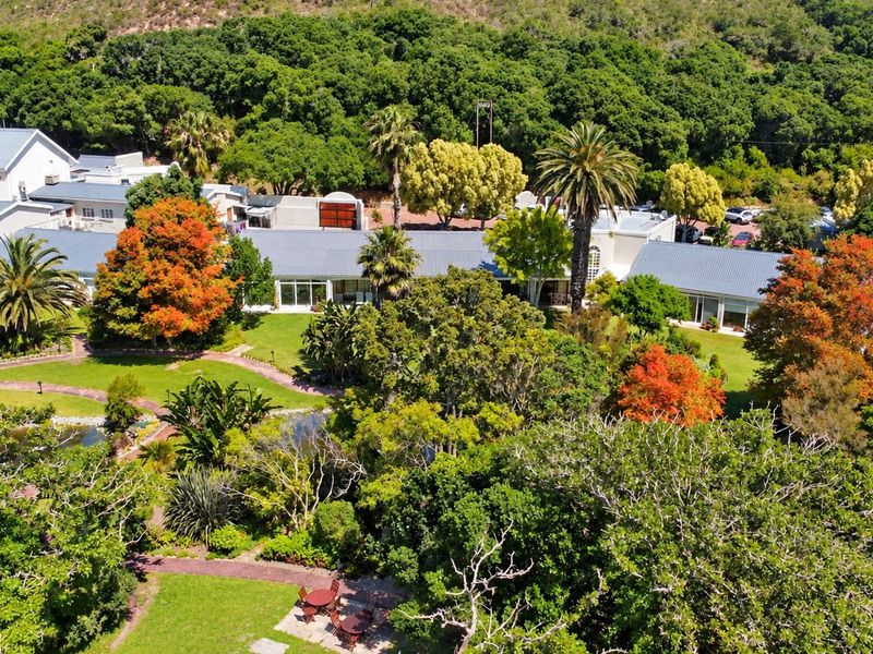 Aerial view of a large property featuring extensive landscaped gardens, mature trees, paved pathways, and multiple building wings with pitched metal roofing.