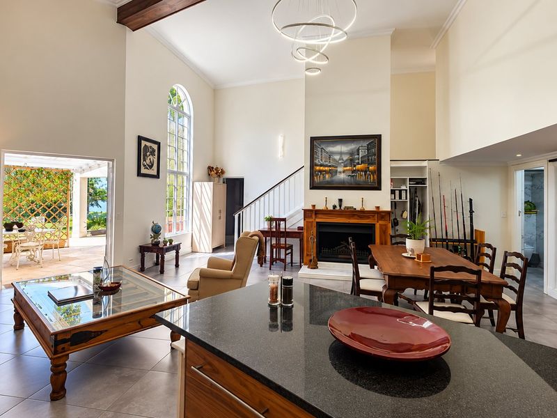 Spacious open-plan living and dining area featuring a granite kitchen island, fireplace, high ceilings with exposed beams, and direct access to an outdoor patio.