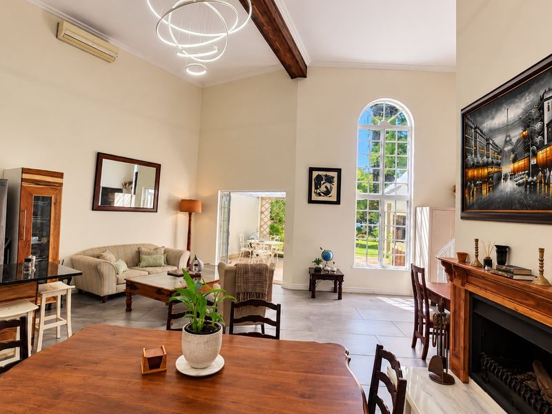 Spacious open-plan living area featuring high ceilings with exposed timber beams, a classic fireplace, and large arched windows providing natural light.
