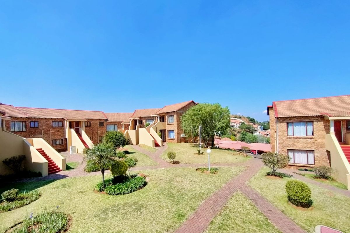 A well-maintained townhouse complex featuring brick facades, tiled roofs, and landscaped communal garden areas with paved walkways.