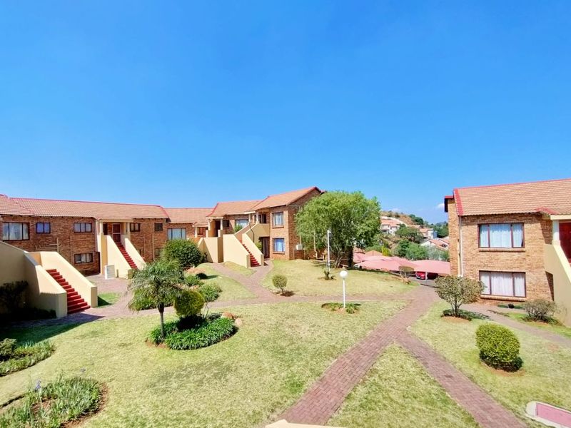 A well-maintained townhouse complex featuring brick facades, tiled roofs, and landscaped communal garden areas with paved walkways.