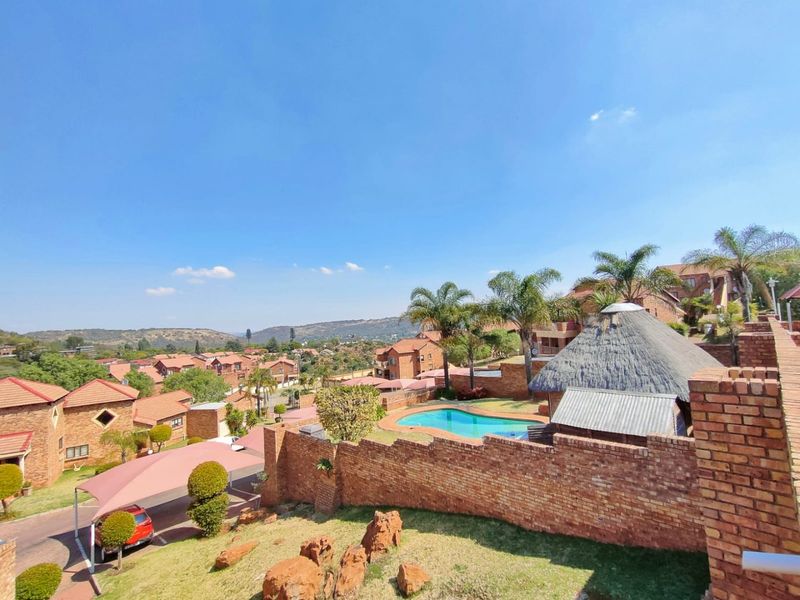 Elevated view overlooking the residential estate, featuring a communal swimming pool, thatched lapa, and brick boundary walls within a landscaped setting.