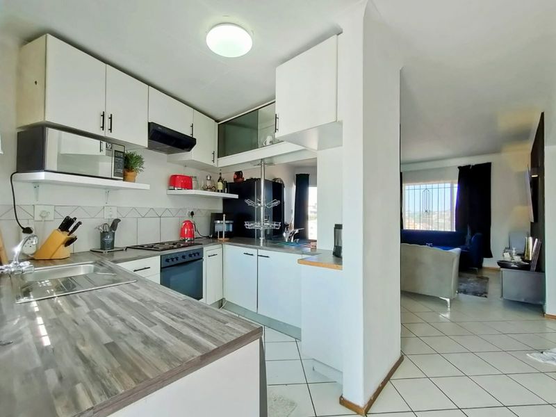 Open-plan kitchen featuring white cabinetry, laminate countertops, and tiled flooring, flowing into a living area with natural light and security bars.