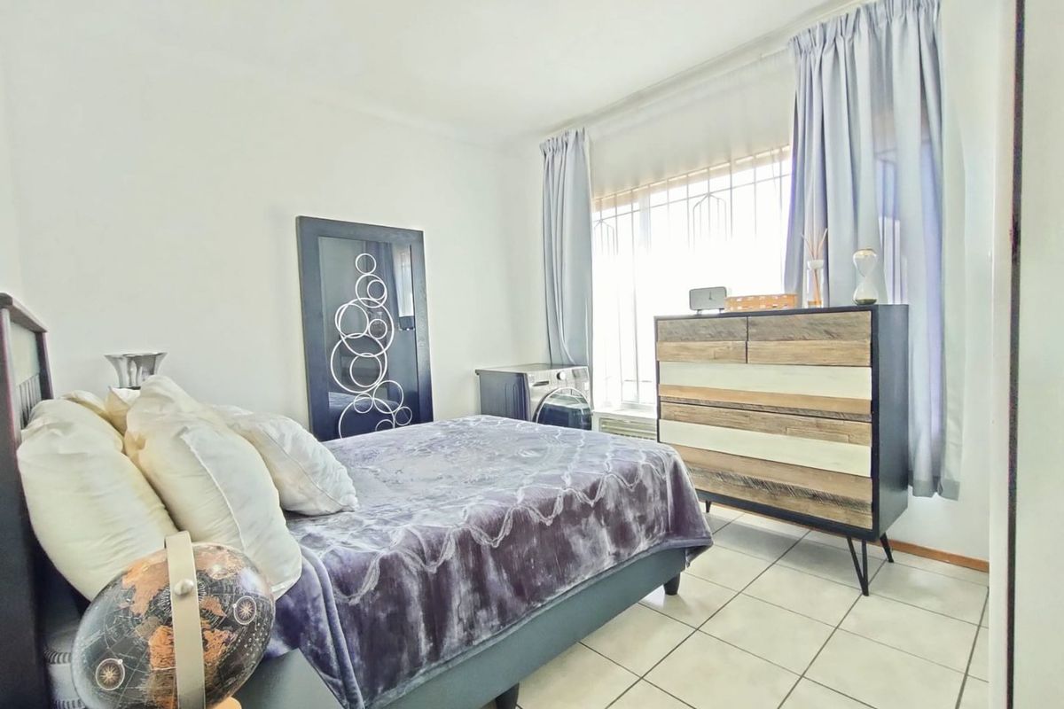 A bedroom featuring tiled flooring and a window fitted with security bars, providing natural light.