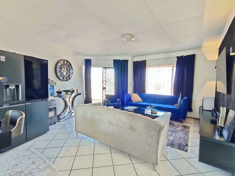 Spacious living room featuring tiled flooring, large windows with security bars, and a sliding door providing access to the exterior.