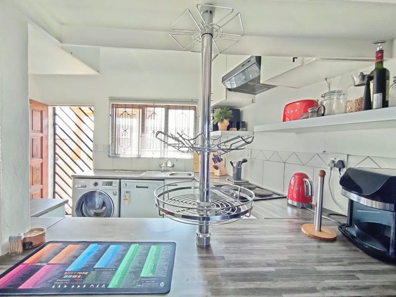 Functional kitchen featuring laminate countertops, built-in hob with extractor fan, and integrated laundry appliance space, with natural light from a window with security blinds.