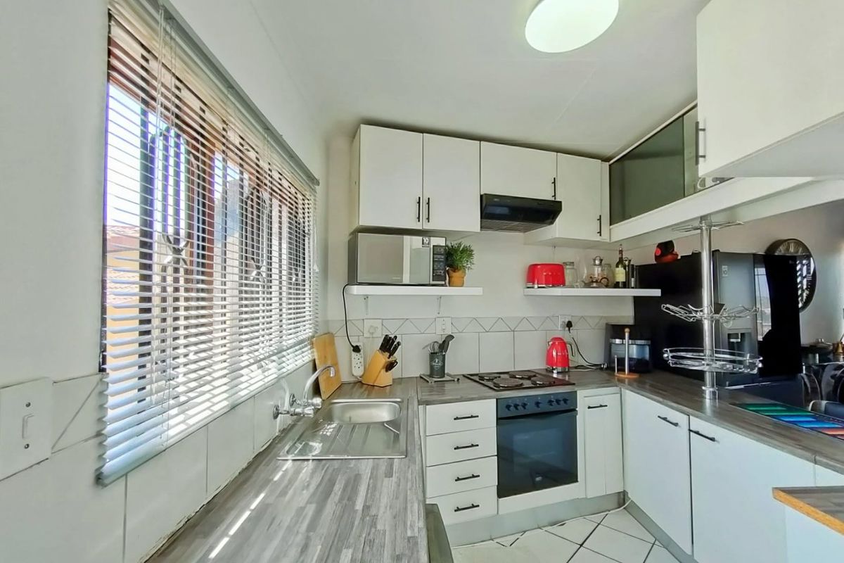 Compact kitchen featuring white cabinetry, laminate countertops, built-in oven with hob, extractor fan, and tiled flooring.