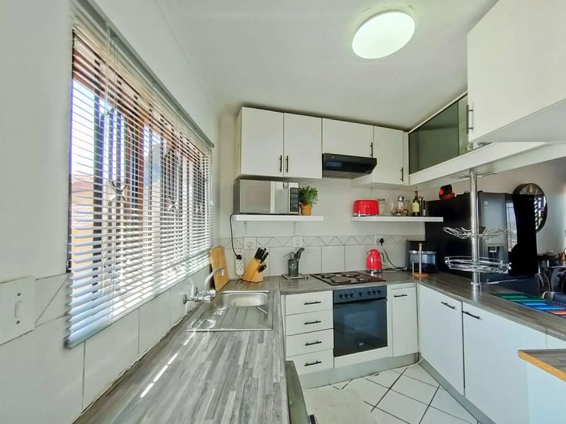 Compact kitchen featuring white cabinetry, laminate countertops, built-in oven with hob, extractor fan, and tiled flooring.
