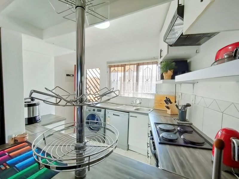 A functional kitchen featuring built-in cabinetry, laminate countertops, an electric hob with extractor fan, and a stainless steel sink with window views.