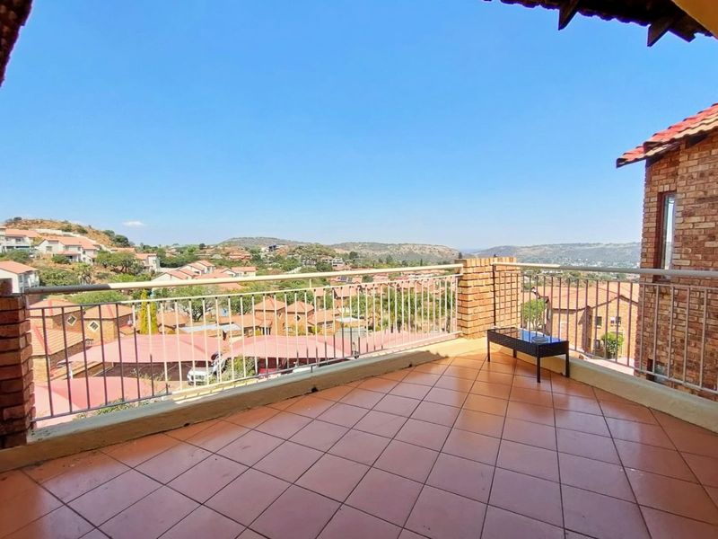 Spacious open balcony featuring tiled flooring, brick pillars, and metal railings, offering expansive elevated views of the surrounding residential estate.