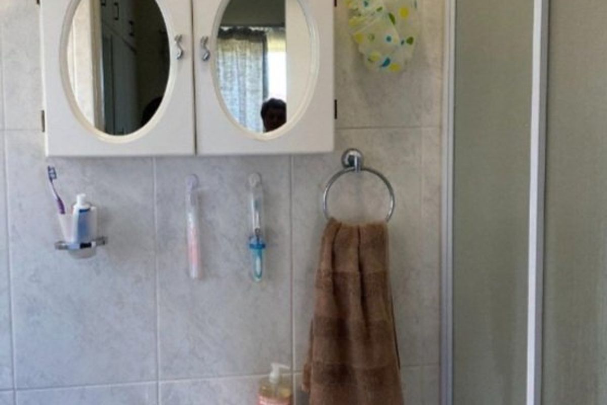 A functional bathroom featuring a pedestal basin with chrome mixer tap, wall-mounted medicine cabinet, and a shower enclosure with tiled walls.