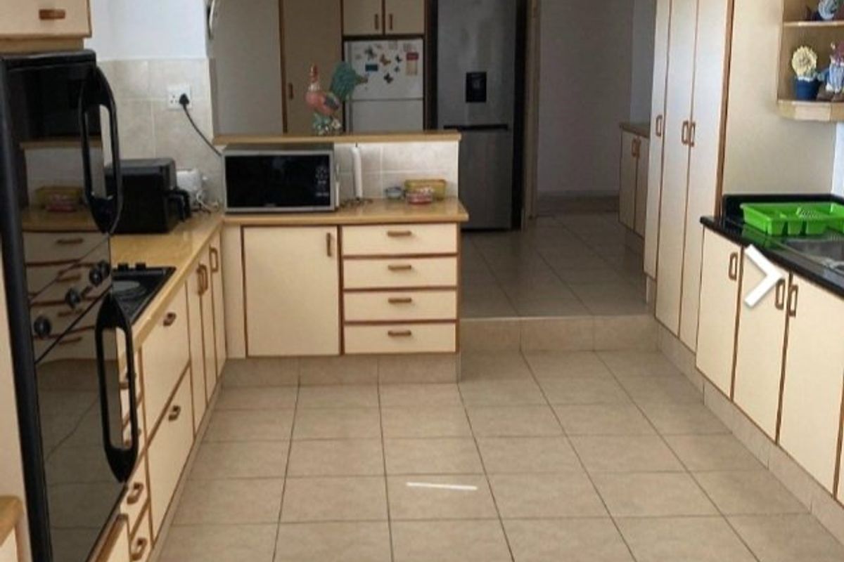 A functional kitchen featuring tiled flooring, ample built-in cabinetry, a built-in oven, and a hob, with a step-up transition to an adjacent utility area.