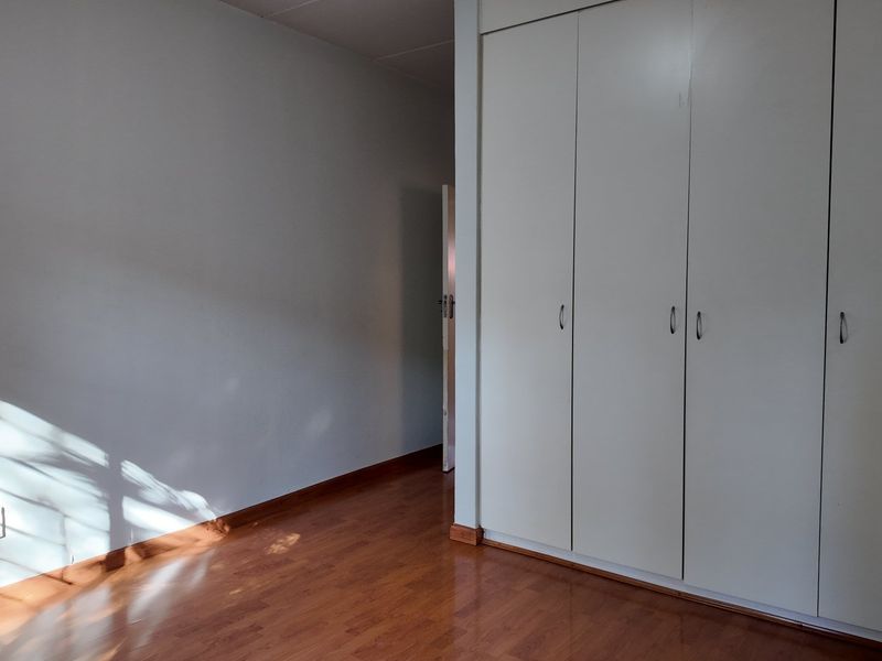 A bright, empty bedroom featuring laminate flooring and ample built-in cupboard storage space.