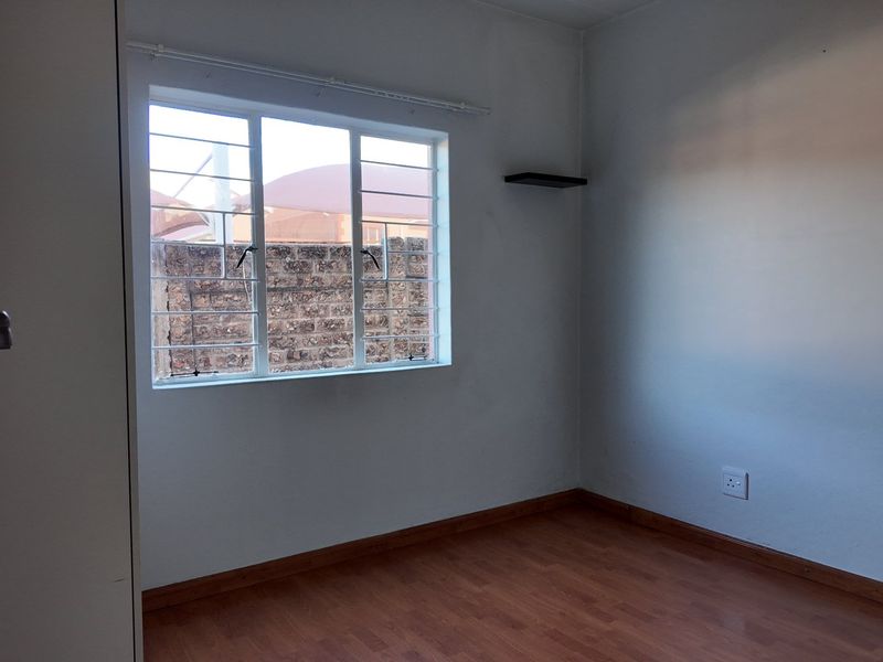 A clean, empty bedroom featuring laminate flooring, a built-in cupboard, and a window fitted with security burglar bars.