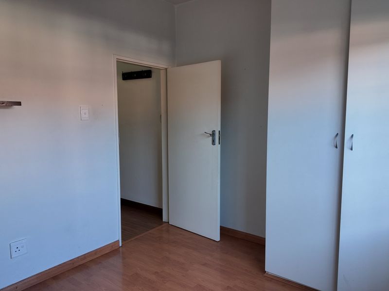 A clean, empty bedroom featuring laminate flooring, built-in cupboards, and floating wall shelves, offering a neutral canvas for personalization.