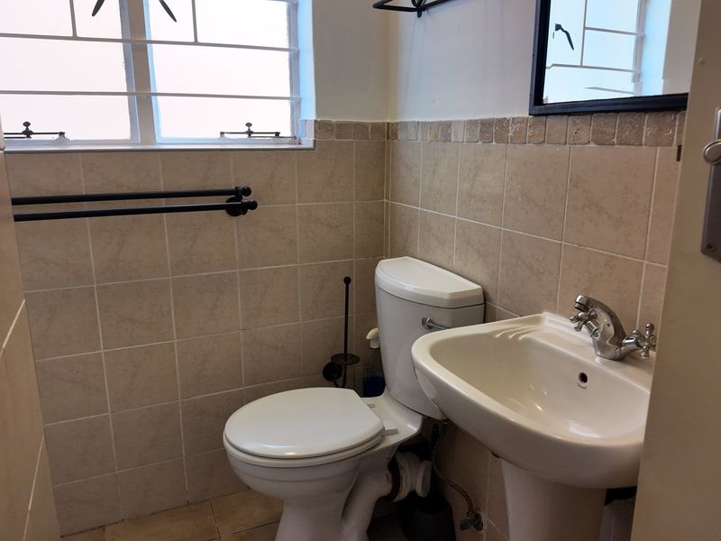 A functional bathroom featuring a pedestal washbasin, toilet, and neutral wall tiling with security bars on the window.