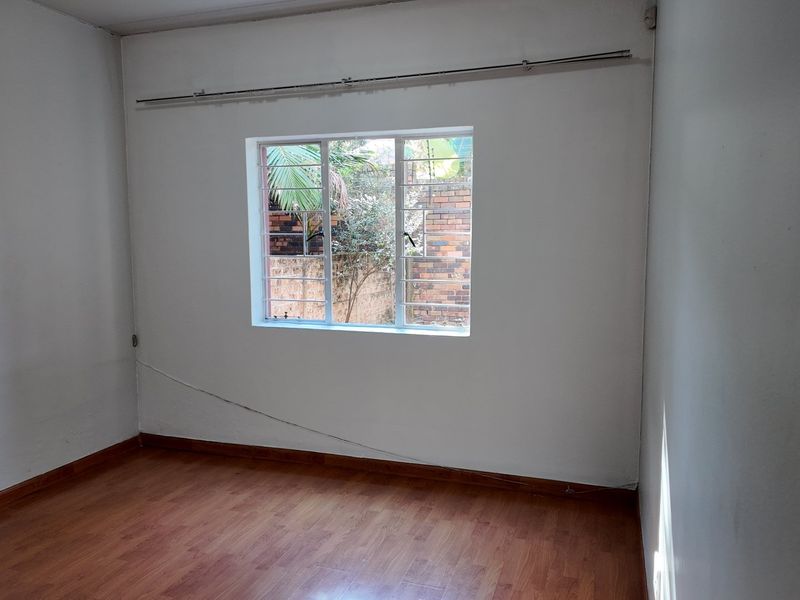 An empty bedroom featuring laminate flooring, a window with security bars, and a curtain rail, ready for personalization.