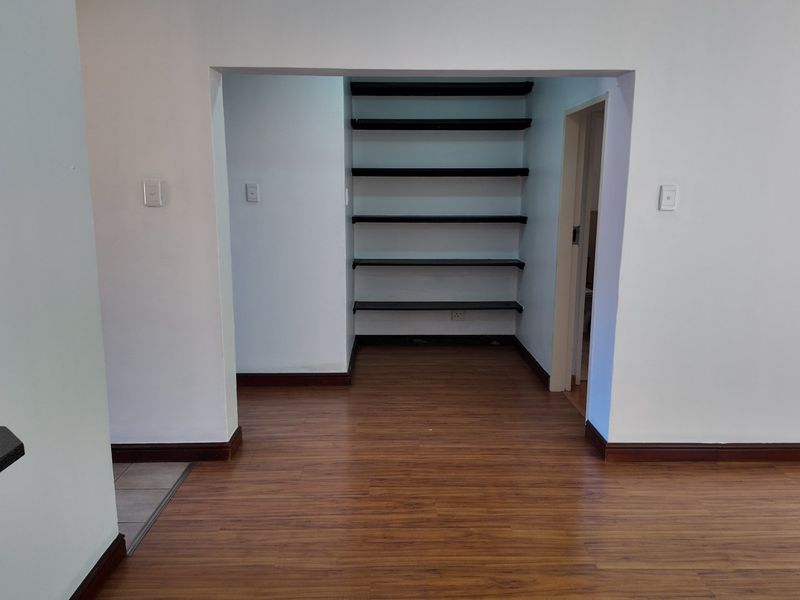A clean, empty utility or storage alcove featuring built-in shelving and wood-look laminate flooring, providing versatile space for organization or a home office setup.