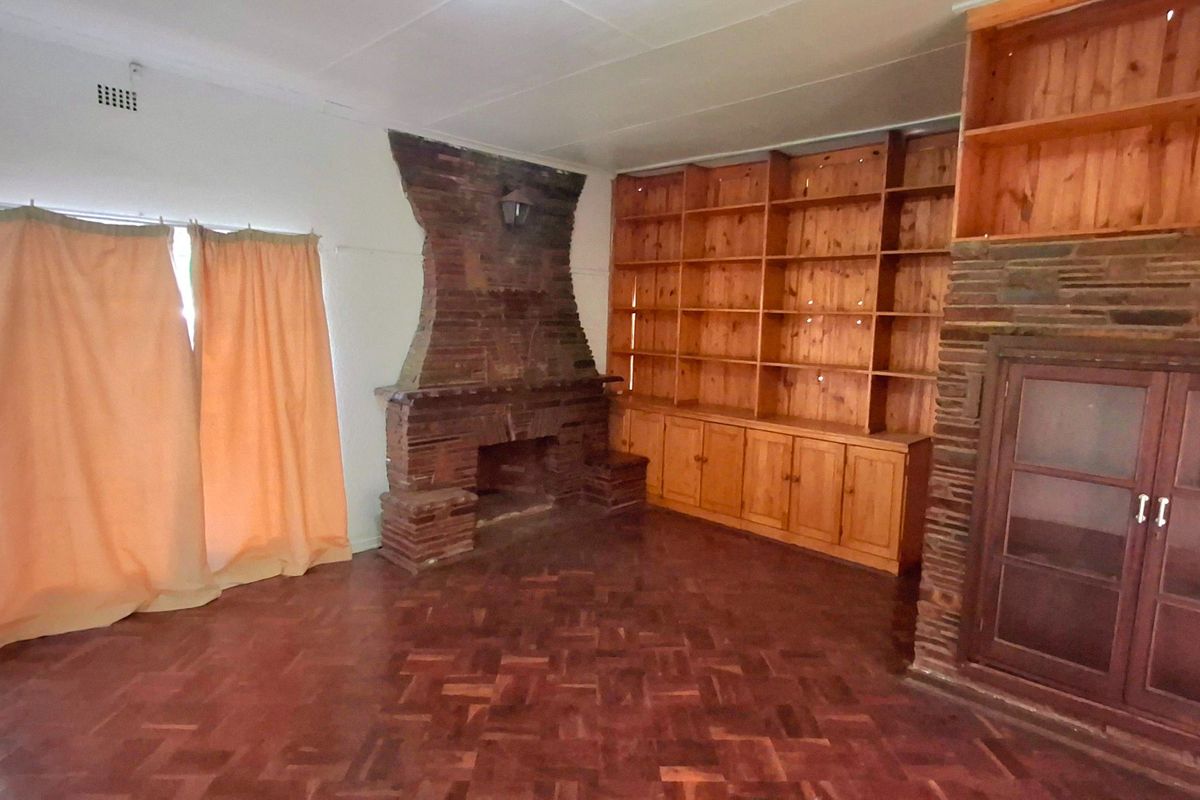 Spacious living room featuring original parquet flooring, a prominent brick fireplace, and extensive built-in wooden shelving and cabinetry.