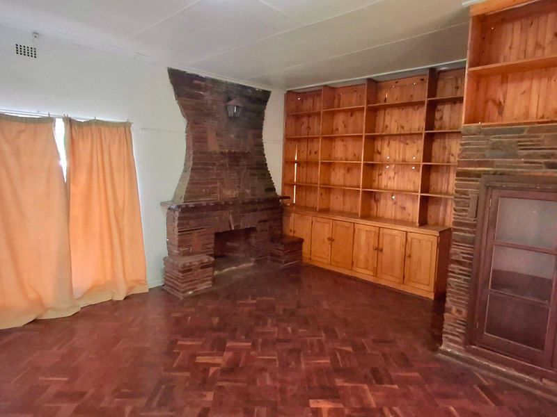 Spacious living room featuring original parquet flooring, a prominent brick fireplace, and extensive built-in wooden shelving and cabinetry.