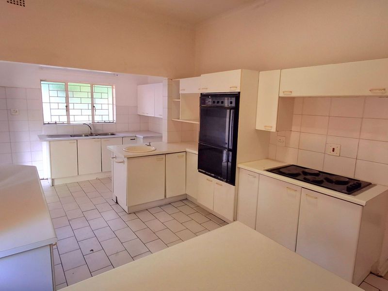 A spacious, dated kitchen featuring white cabinetry, a double wall oven, electric hob, and tiled flooring, offering significant potential for a modern renovation.