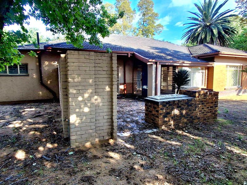 Rear view of the house featuring a paved patio area with a built-in brick braai and established garden surroundings.