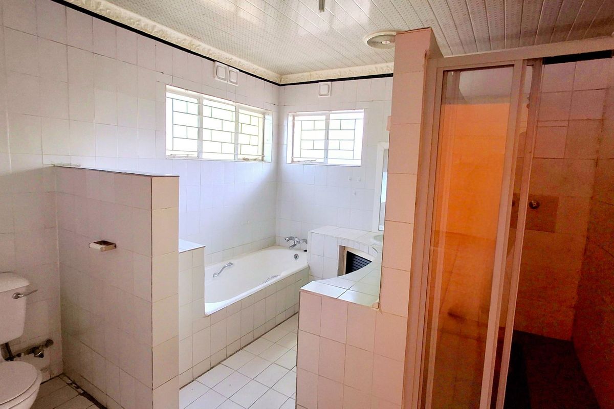 A spacious, dated bathroom featuring a built-in bathtub, separate shower enclosure, and toilet, finished with white wall and floor tiles.