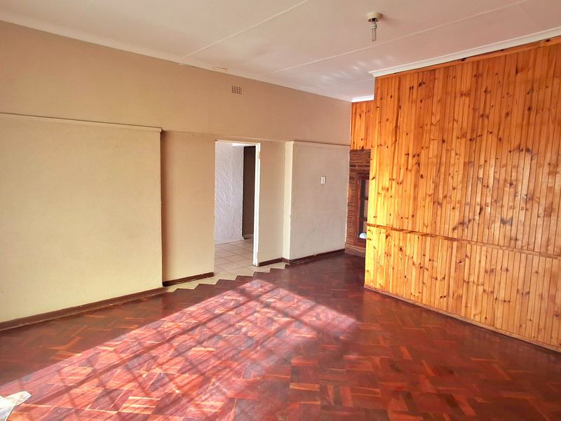 Spacious living area featuring traditional parquet flooring and decorative timber wall paneling, offering a blank canvas for renovation and modern interior design updates.