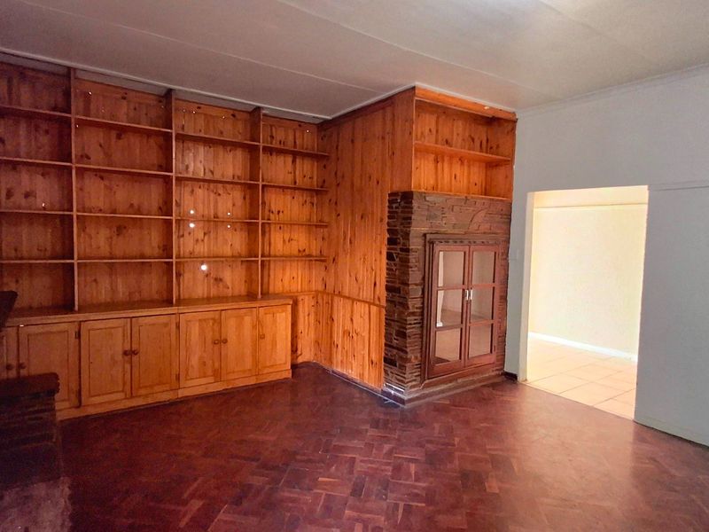 Spacious living room featuring classic parquet flooring, extensive built-in wooden shelving, and a characterful stone fireplace surround with a glass display cabinet.