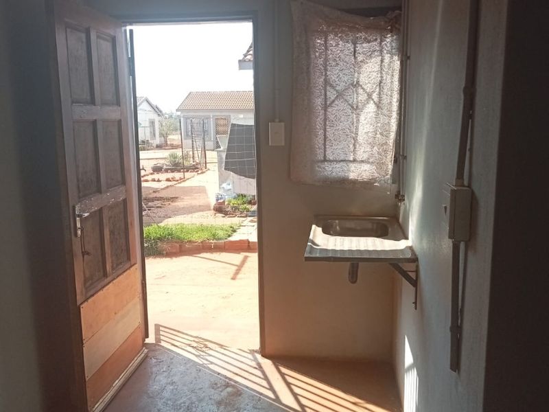 A functional utility or scullery area featuring a wall-mounted sink, exposed electrical conduits, and direct access to the exterior through a timber door.