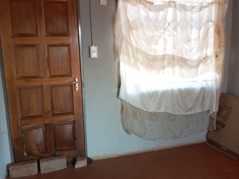 A vacant bedroom featuring a timber door and basic wall finishes, requiring cosmetic updates and repairs to the wall and flooring.