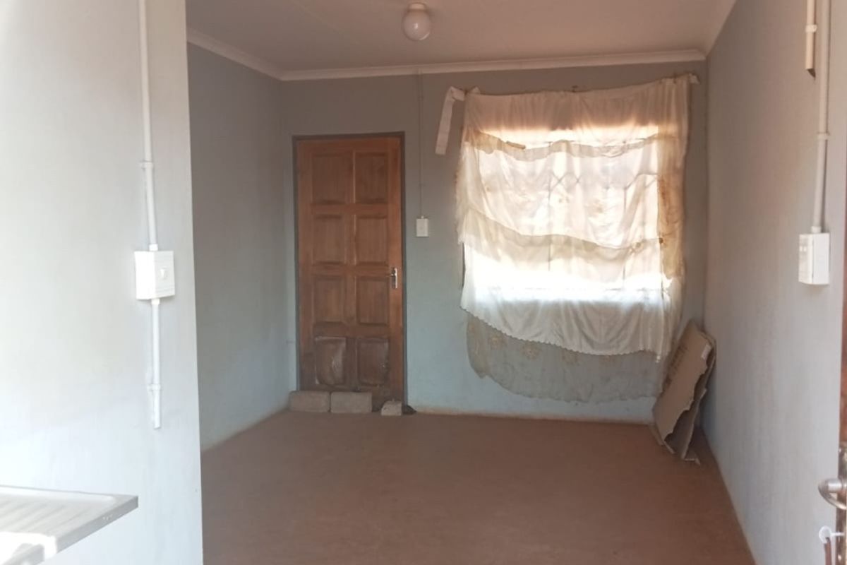 An empty living area featuring exposed electrical conduit, a timber door, and coved ceilings, presenting a blank canvas for renovation and interior design updates.