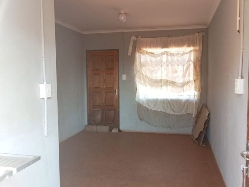 An empty living area featuring exposed electrical conduit, a timber door, and coved ceilings, presenting a blank canvas for renovation and interior design updates.