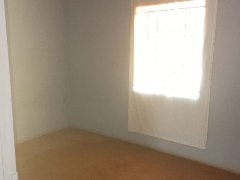An empty bedroom featuring plain walls, a window with security bars, and unfinished flooring, offering a blank canvas for renovation.