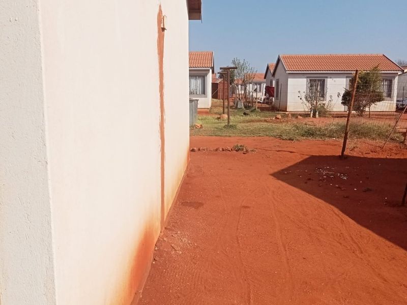 A view of the side and rear exterior of the house showing a plastered wall with visible staining and an unlandscaped dirt yard.