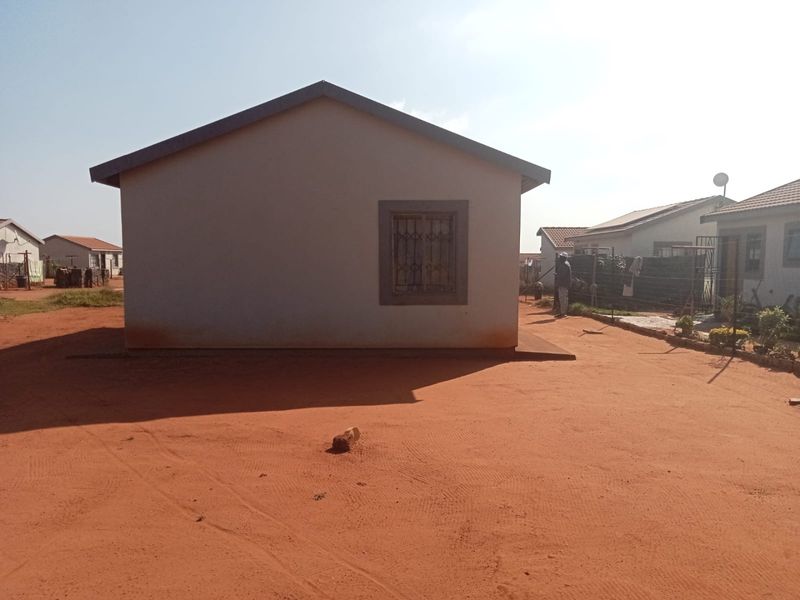 A view of the rear exterior of the house featuring a tiled roof and a window with security bars, set on a dirt plot.