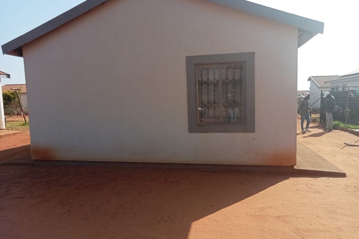 Side elevation of a residential house featuring plastered walls, a single window with security bars, and concrete roof tiles.