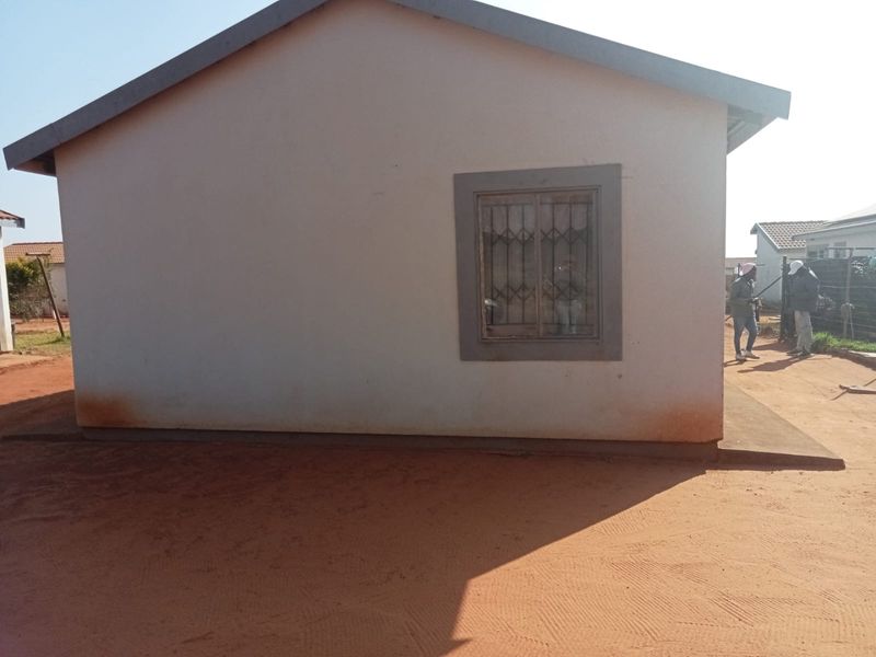 Side elevation of a residential house featuring plastered walls, a single window with security bars, and concrete roof tiles.