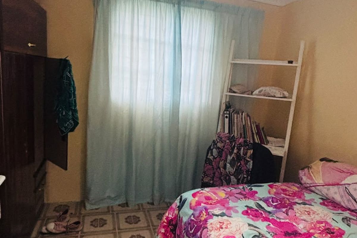 A bedroom featuring tiled flooring, a built-in wardrobe, and a window with curtains. The space requires cosmetic updates to improve its overall condition.