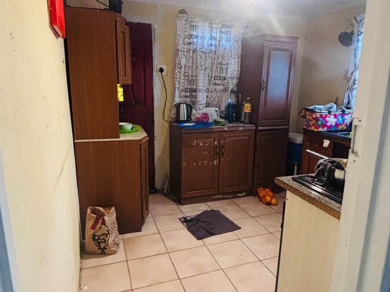 A dated kitchen featuring built-in wooden cabinetry, tiled flooring, and an extractor fan, requiring cosmetic updates and repairs to wall finishes.