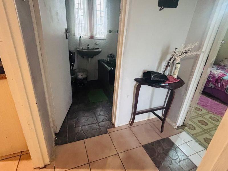 A view of a residential hallway connecting to a bathroom and bedroom, featuring tiled flooring and standard interior door frames.