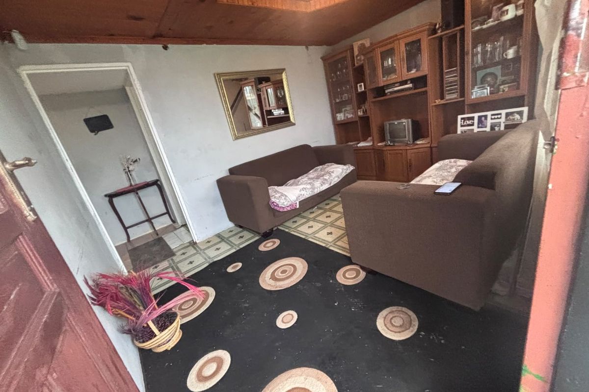 A dated living room featuring a timber ceiling, vinyl flooring, and a built-in wall unit, requiring cosmetic updates to modernize the space.