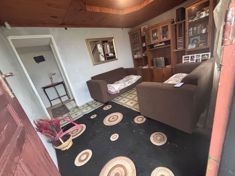 A dated living room featuring a timber ceiling, vinyl flooring, and a built-in wall unit, requiring cosmetic updates to modernize the space.