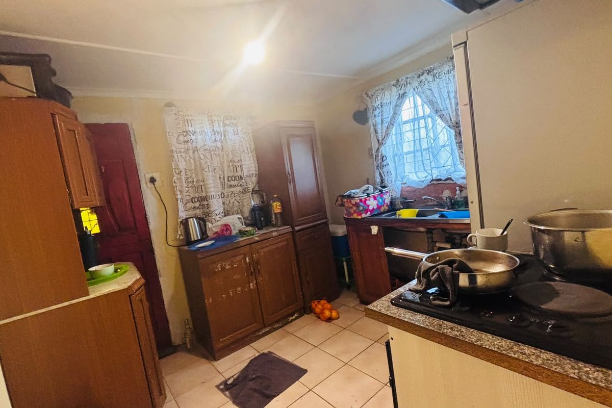 A functional kitchen featuring built-in wooden cabinetry, a sink, and a hob, with tiled flooring and a security gate on the door.