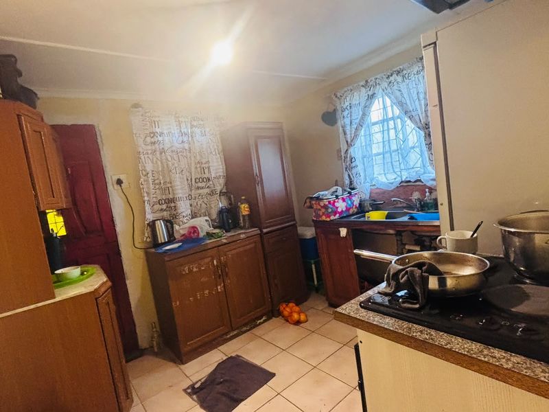 A functional kitchen featuring built-in wooden cabinetry, a sink, and a hob, with tiled flooring and a security gate on the door.