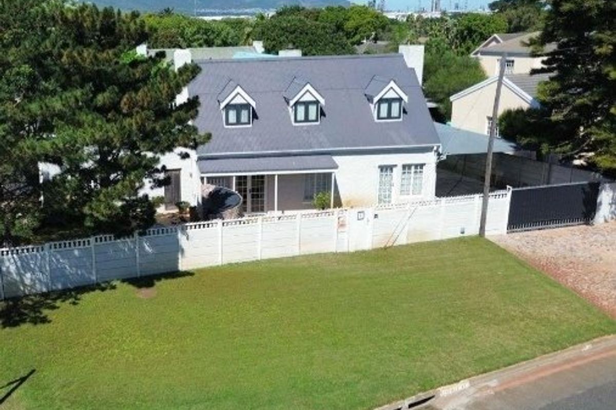 Aerial view of a residential property featuring a metal roof with dormer windows, a large front lawn, and a secure boundary wall with driveway access.