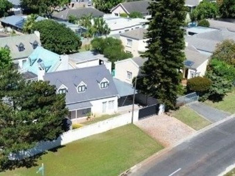Aerial view of a residential property featuring a pitched roof, dormer windows, a paved driveway, and a secure perimeter wall.