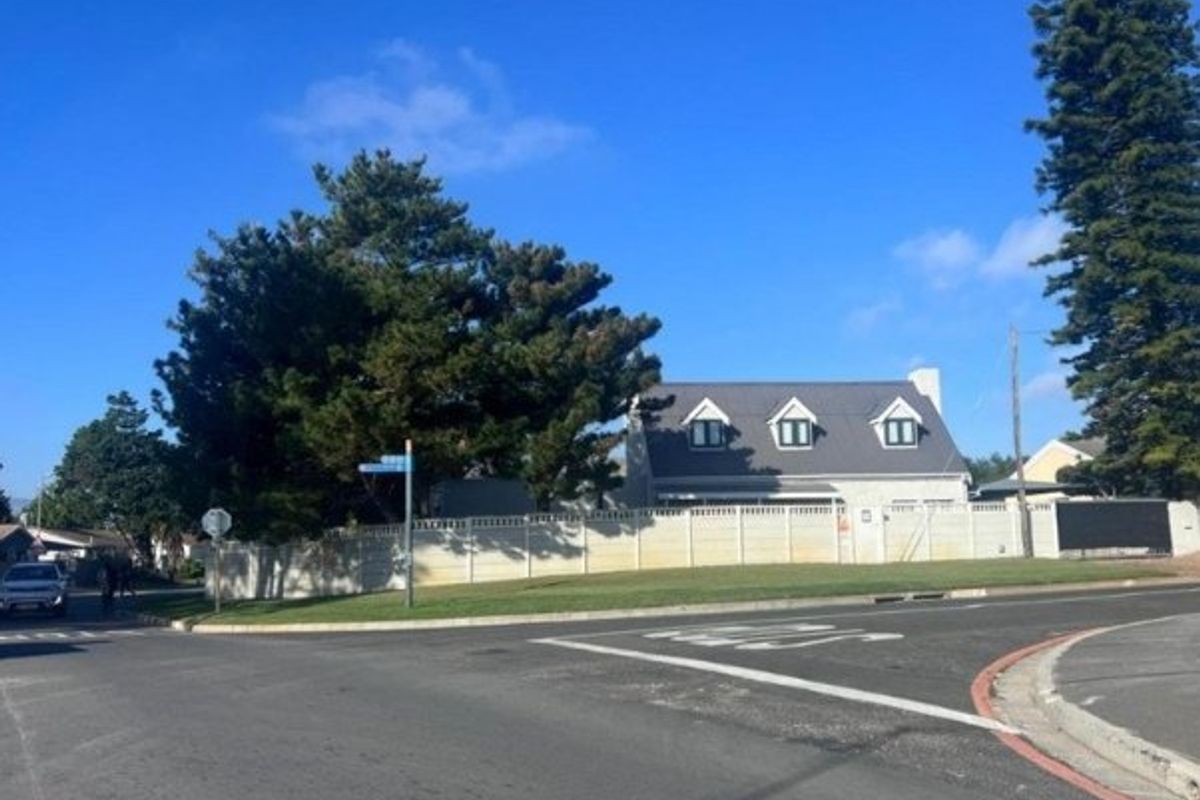 Street view of a residential property featuring a perimeter fence, pitched roof, and dormer windows, situated on a corner lot.