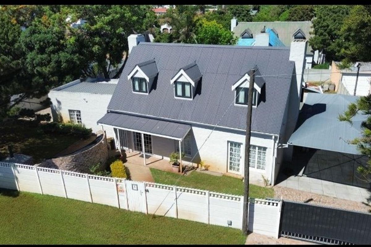 Aerial view of a residential property featuring a pitched metal roof with dormer windows, a front garden, and a covered carport area.