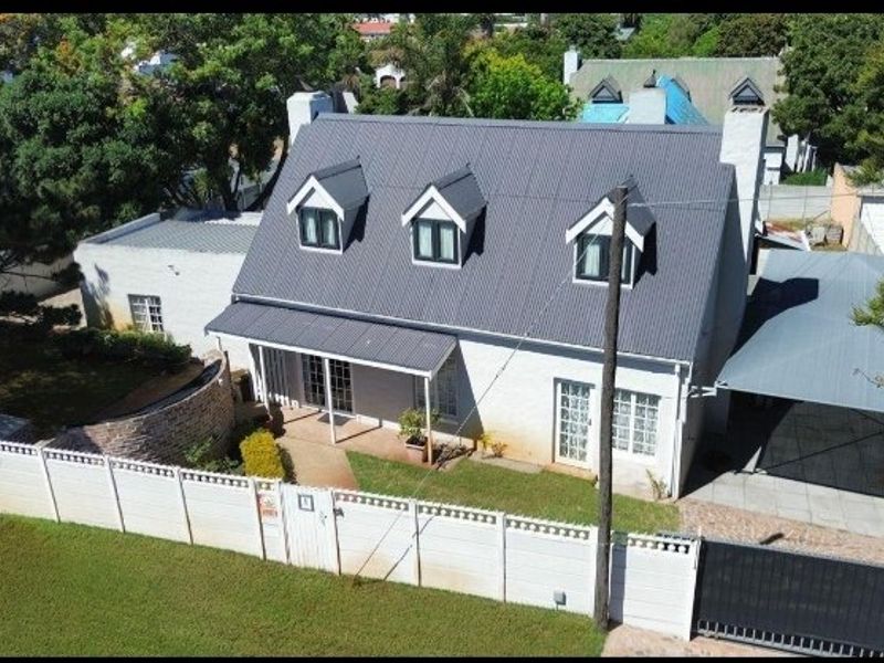 Aerial view of a residential property featuring a pitched metal roof with dormer windows, a front garden, and a covered carport area.